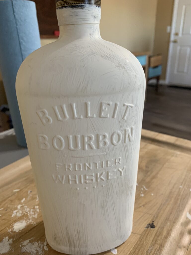 Whiskey bottle with one coat of white paint.
